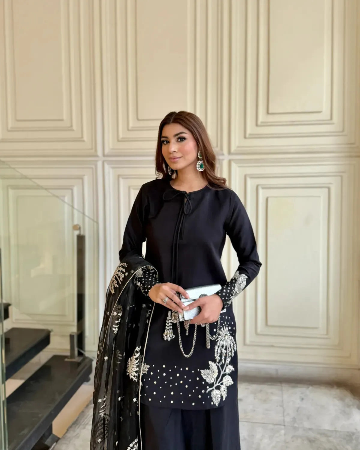 Woman in black outfit with floral details standing in a room with decorative walls.