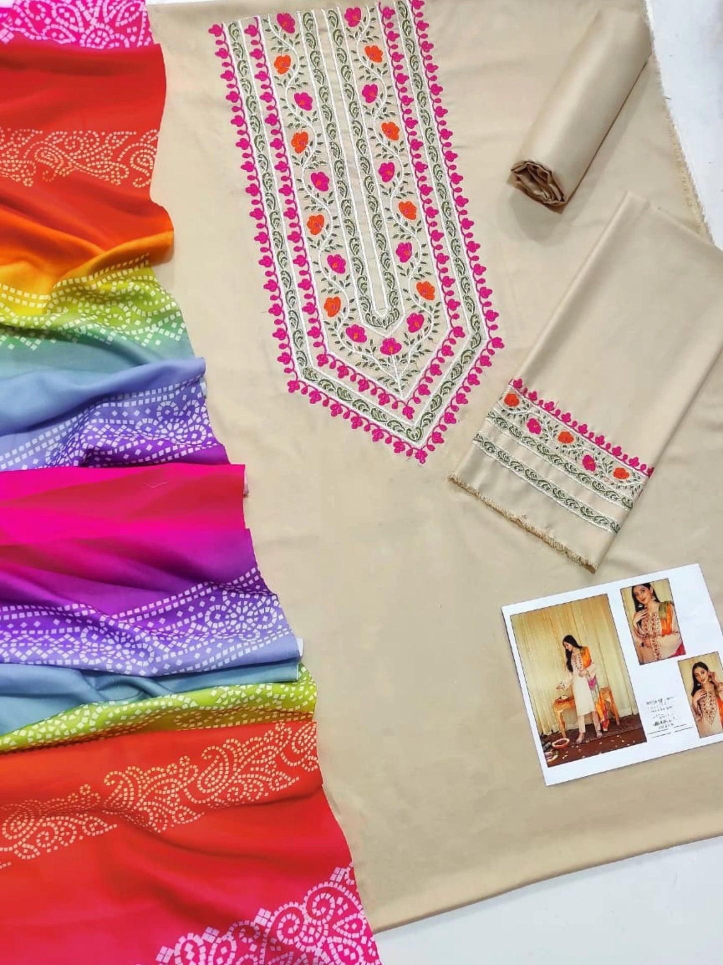 Colorful fabric with embroidered patterns and a beige fabric roll on a white background.