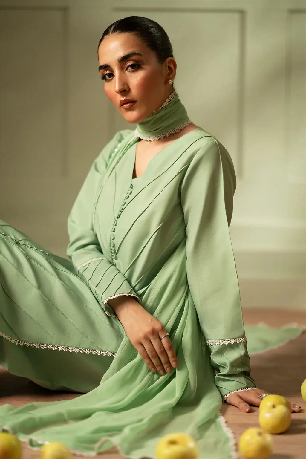 Woman in a light green traditional outfit sitting on the floor with apples around her.