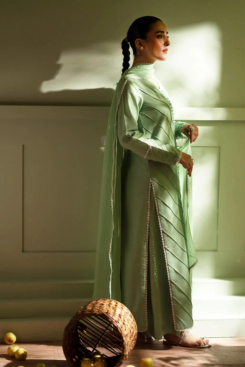 Woman in a light green traditional outfit standing in a softly lit room.