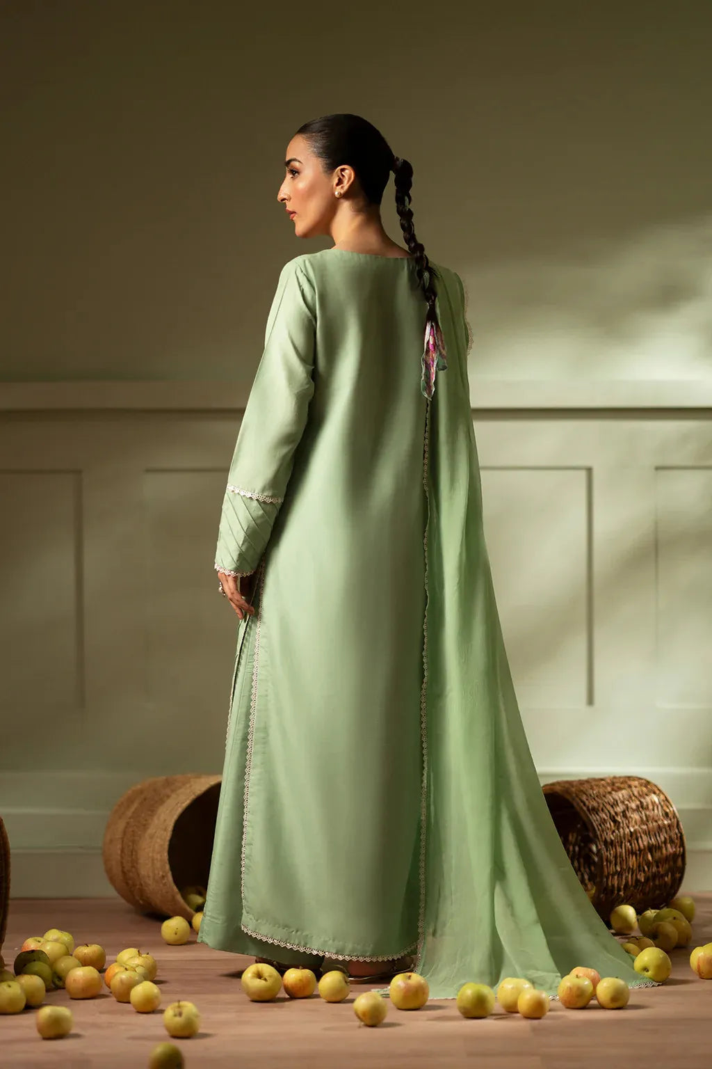 Woman in a long green dress standing among scattered fruits with a neutral background