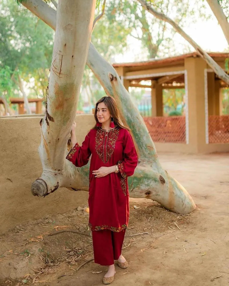 Woman in a red traditional outfit standing next to a large tree in an outdoor setting.