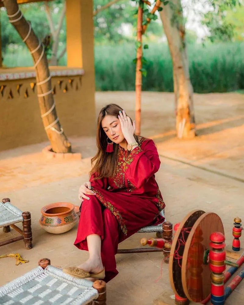 Woman in a red traditional outfit sitting outdoors with rustic elements.