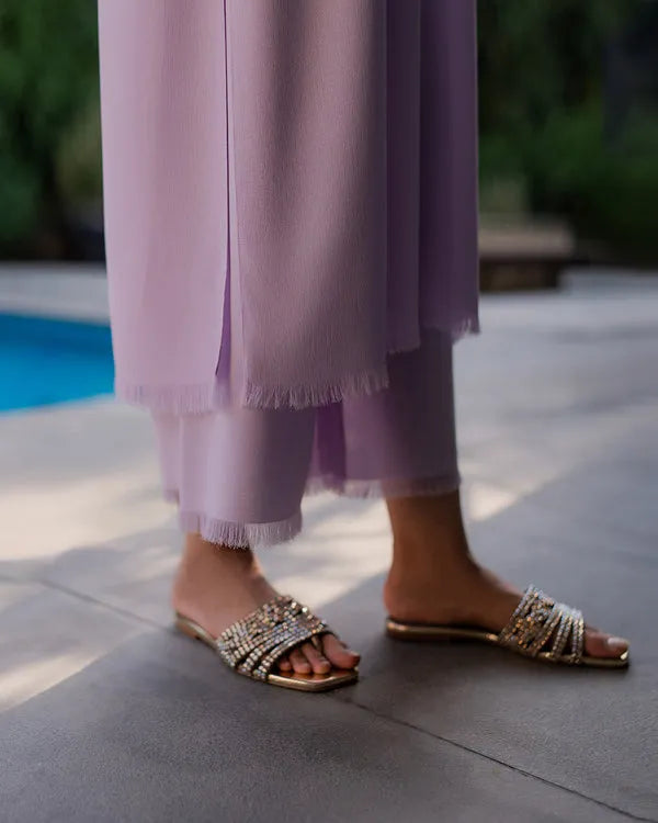 Person wearing embellished sandals and light purple pants by a poolside.