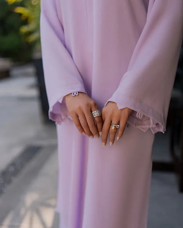 Person wearing a light purple dress with ruffled sleeves, holding hands with another person.