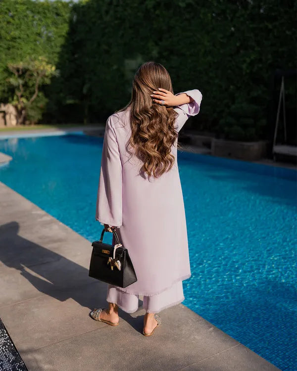 Woman in a light pink coat standing by a poolside