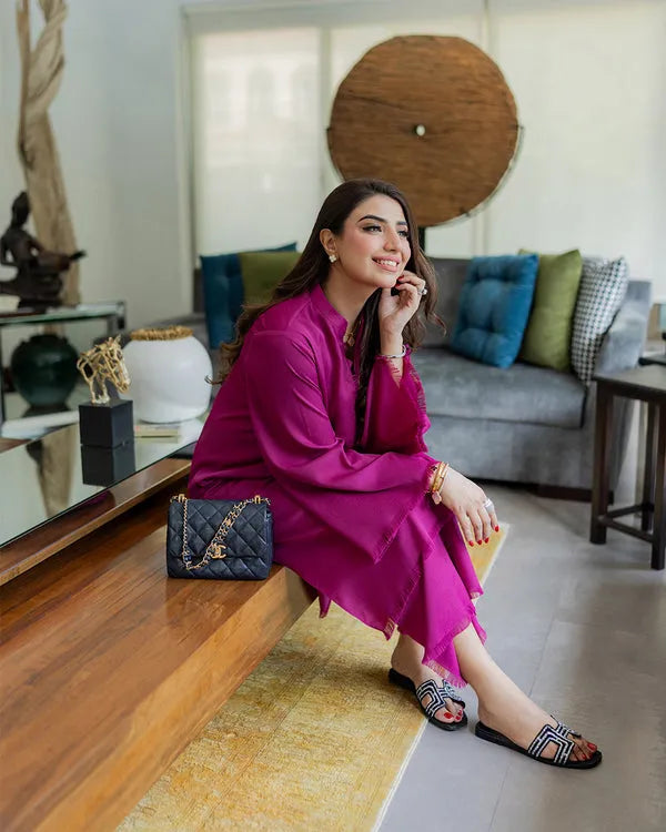Woman in a bright pink outfit sitting on a wooden bench in a modern living room.