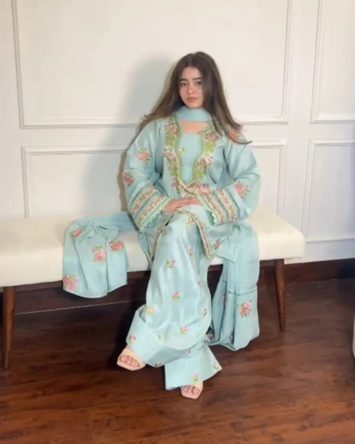 Woman in a light blue embroidered traditional outfit sitting on a bench.