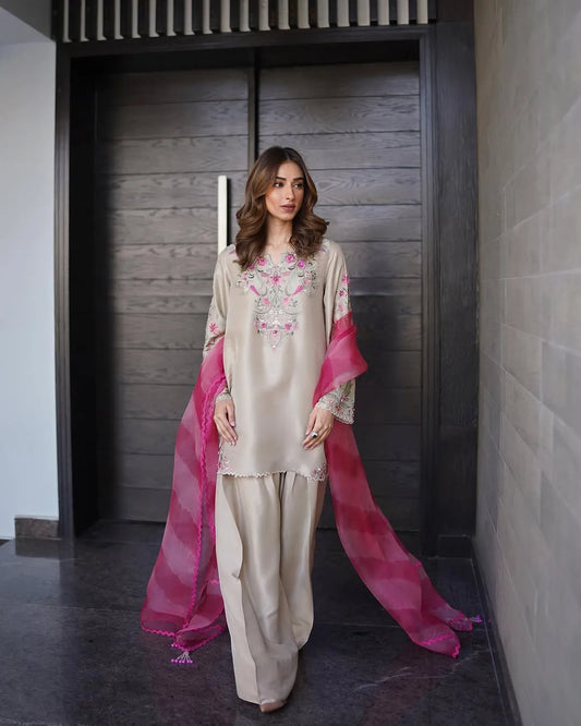 Woman in a traditional outfit with pink dupatta standing indoors.