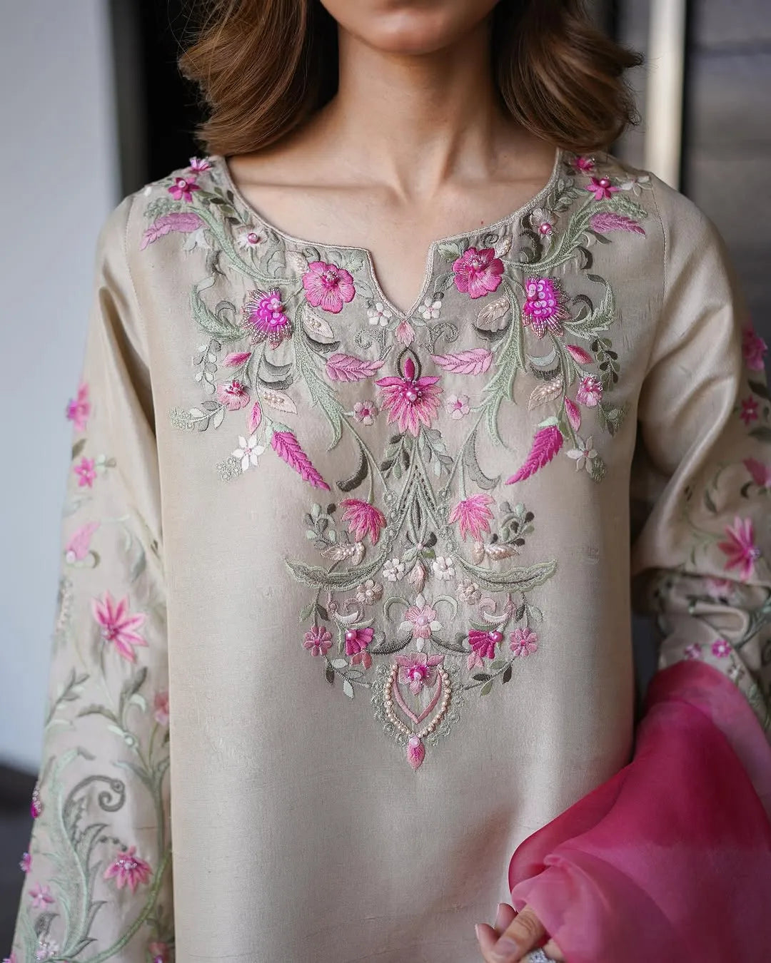 Beige embroidered blouse with pink flowers and green details, held by a person.