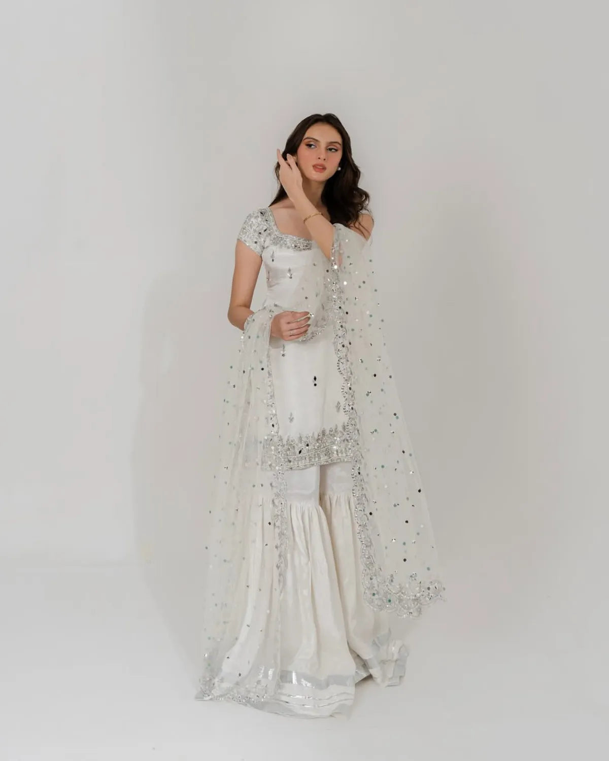 Woman wearing a white saree with silver embroidery on a plain background