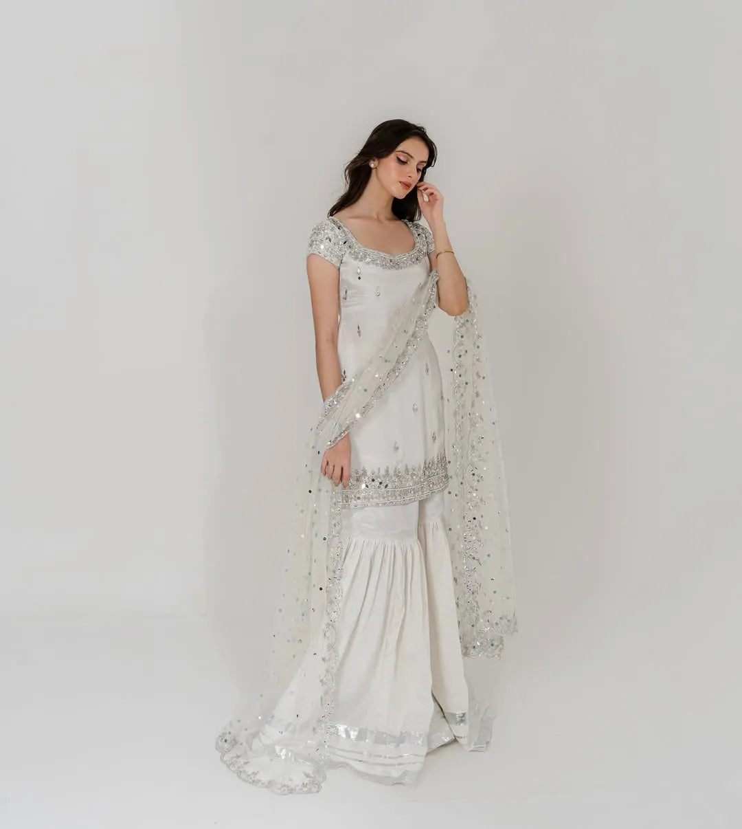 Woman wearing a white saree with intricate designs on a plain background