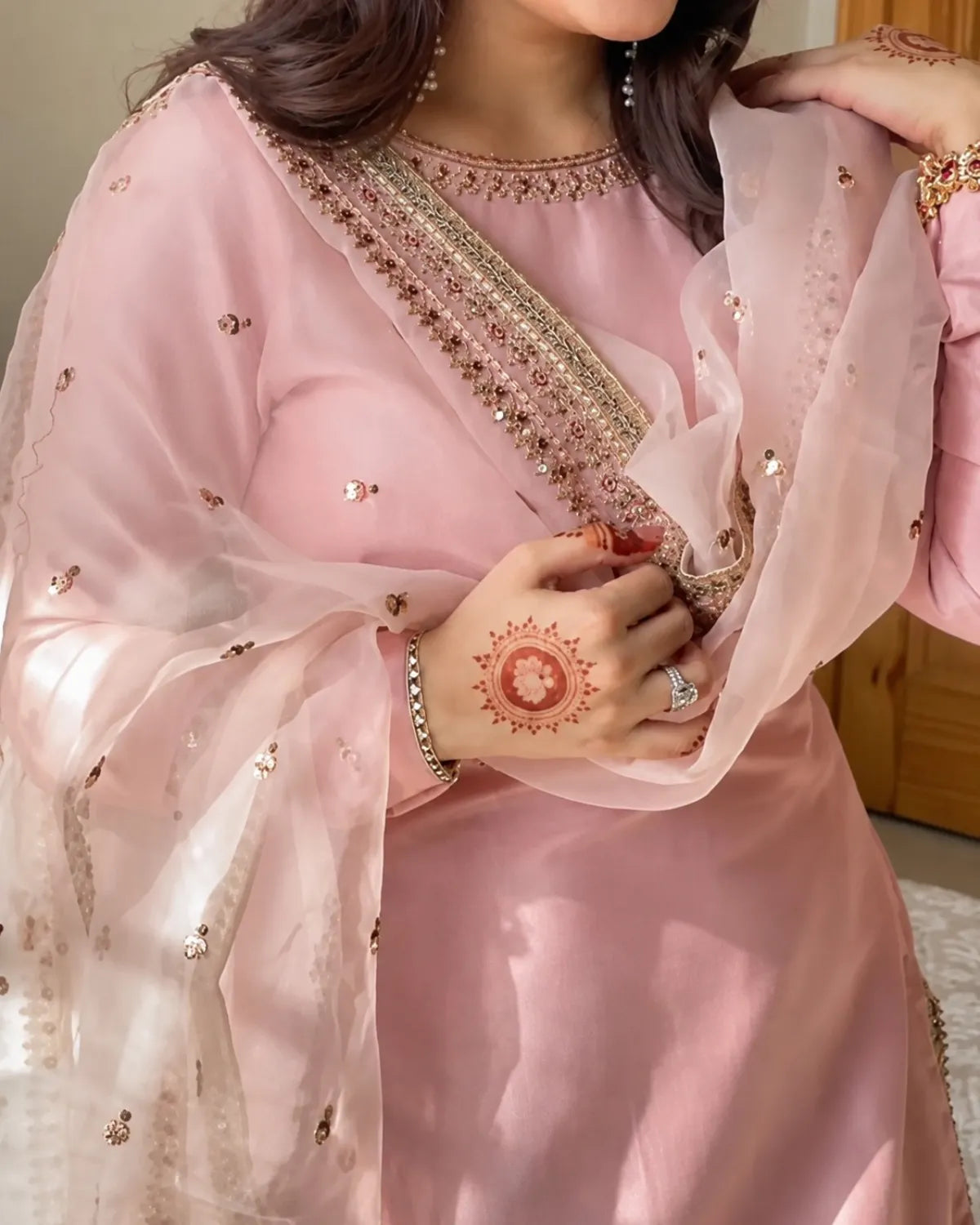 Person wearing a pink traditional outfit with intricate designs, holding a hand with a red henna design.