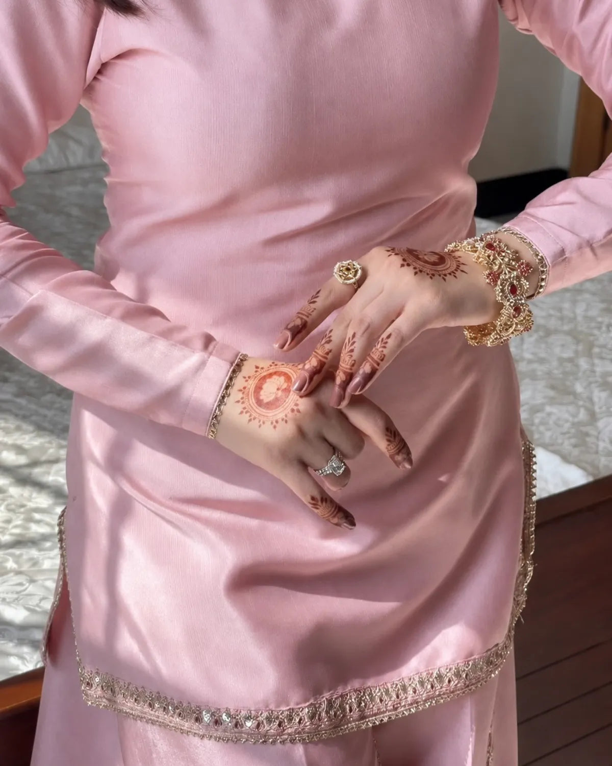 Person wearing a pink traditional outfit with intricate henna designs on hands and rings.