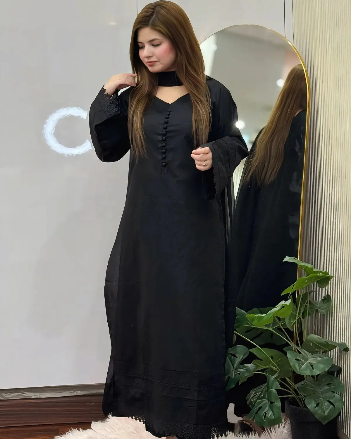Woman wearing a black dress standing in front of a mirror.