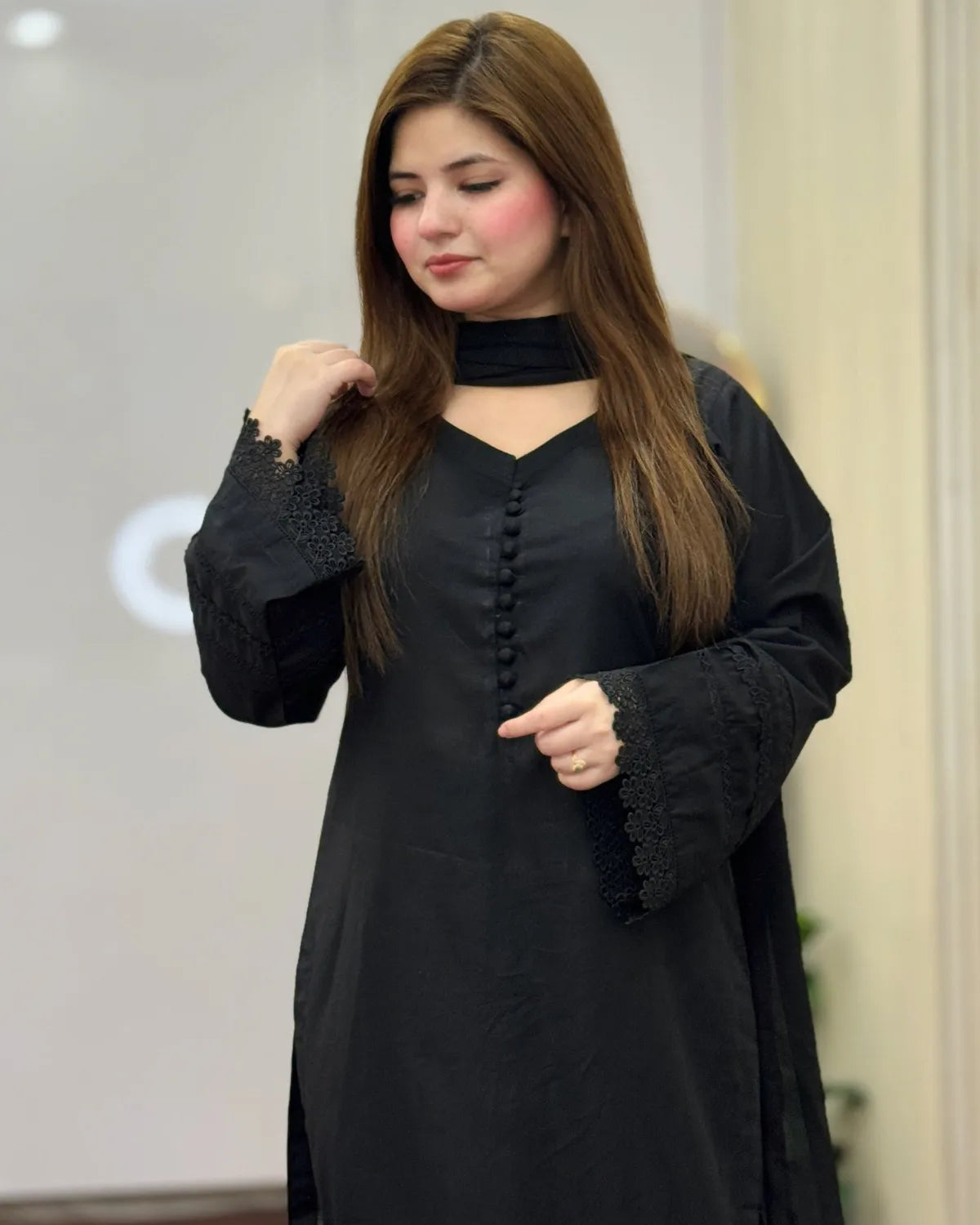 Woman wearing a black outfit with lace details indoors.