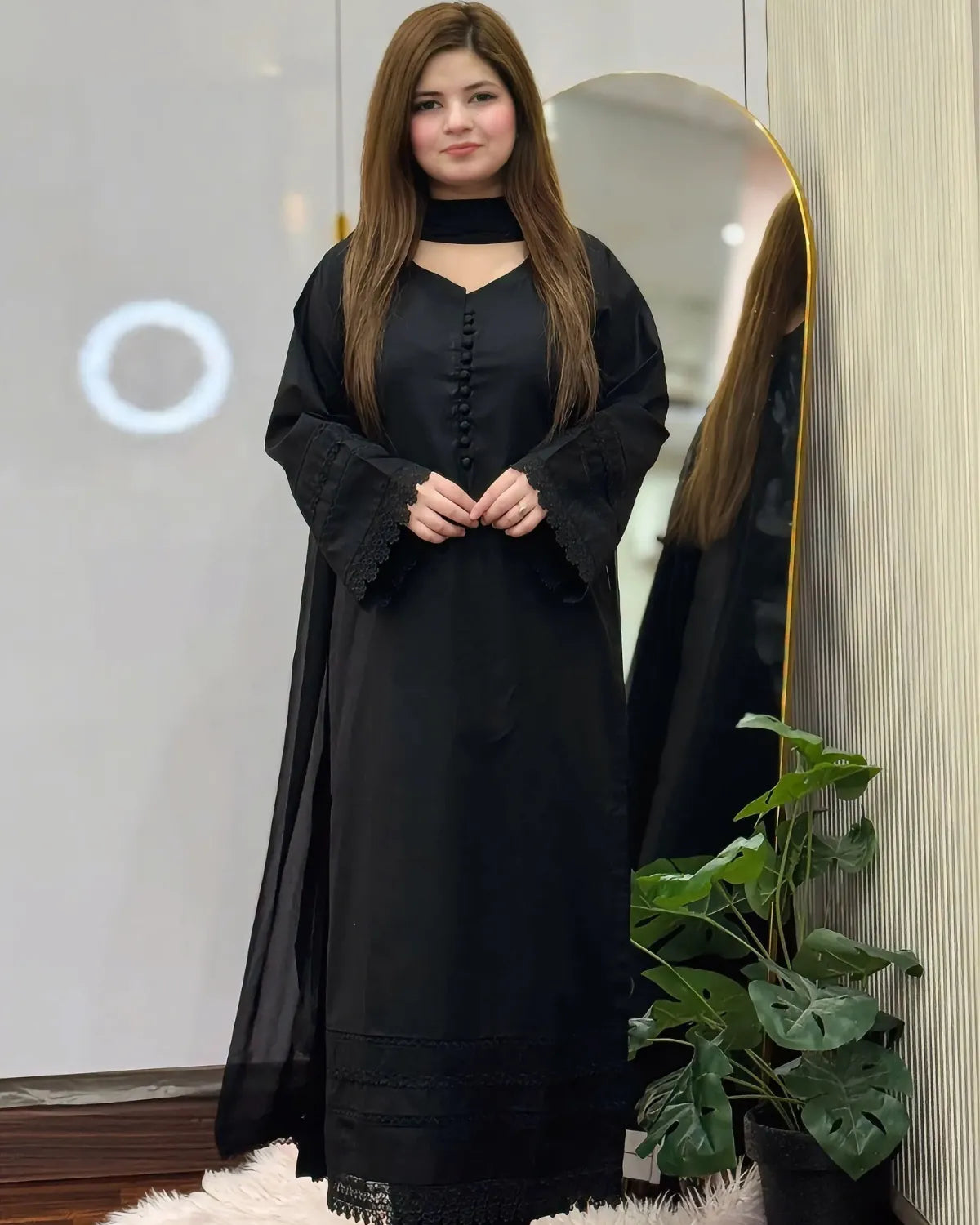 Woman wearing a black outfit with a sheer overlay in front of a mirror.