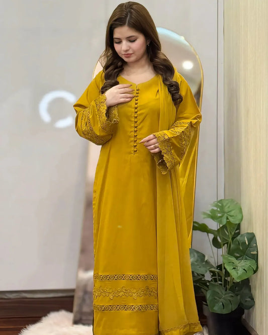 Woman wearing a yellow traditional outfit with intricate designs, standing indoors.