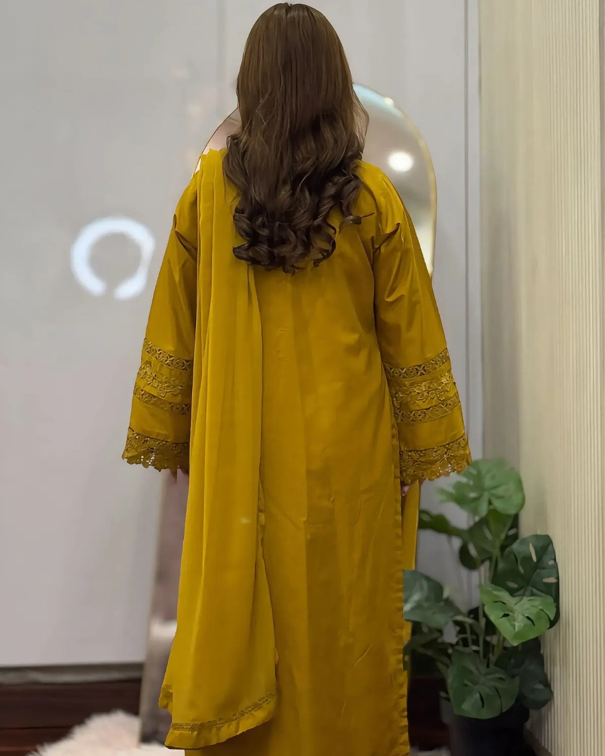 Person wearing a yellow outfit with lace details in a room with a plant.