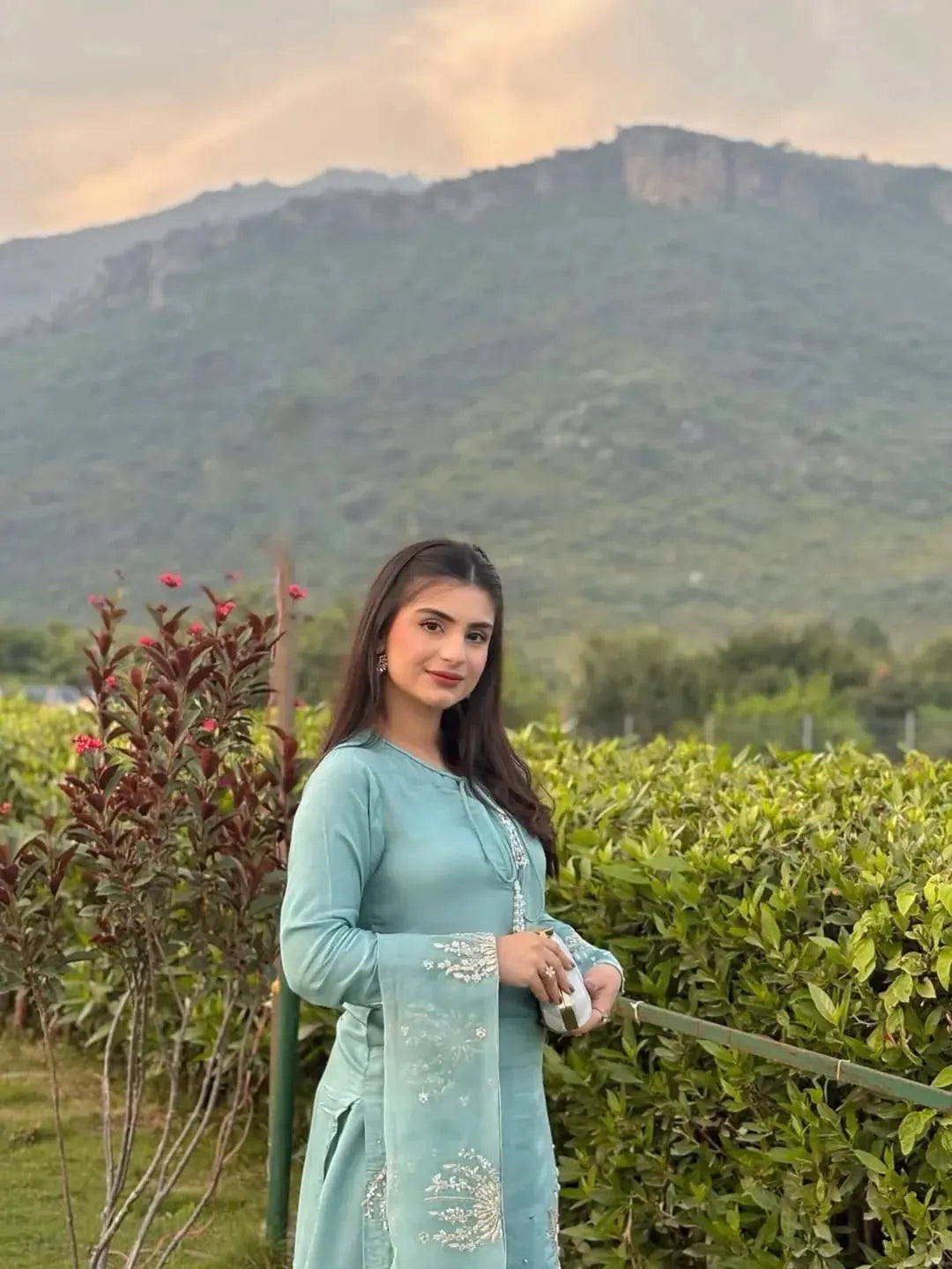 Woman in a light blue outfit standing in a field with mountains in the background