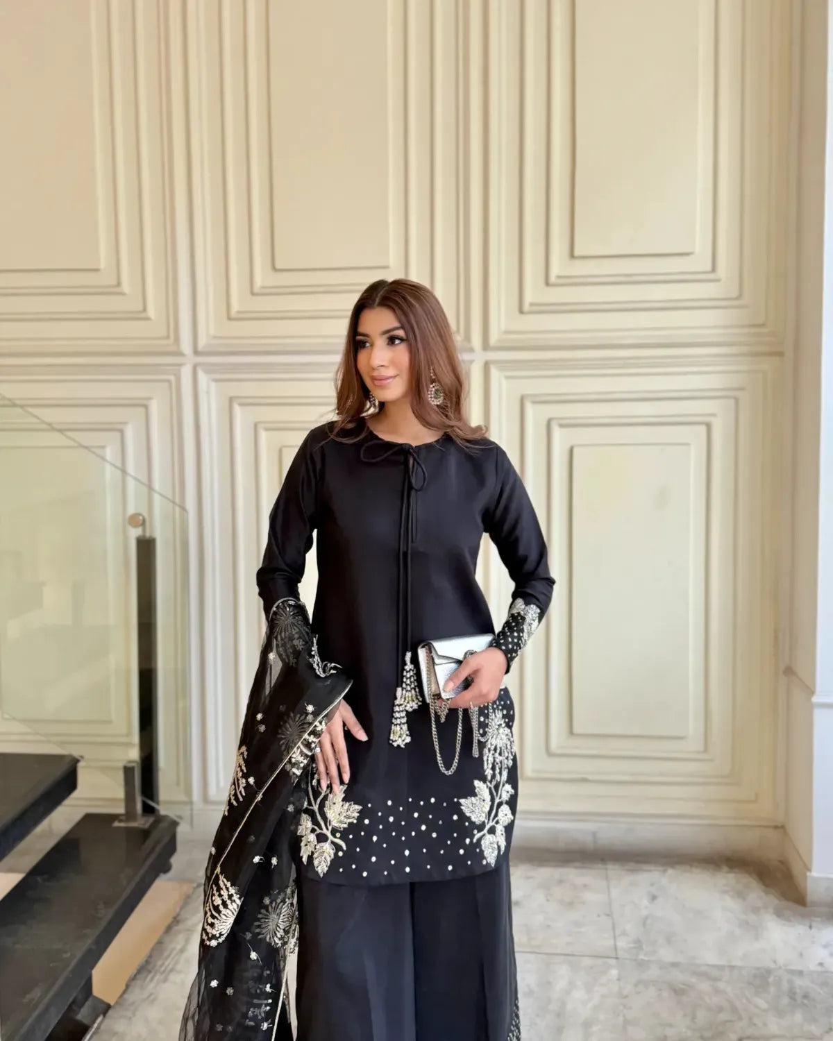 Woman in a black outfit with floral embellishments standing in a room with decorative walls.