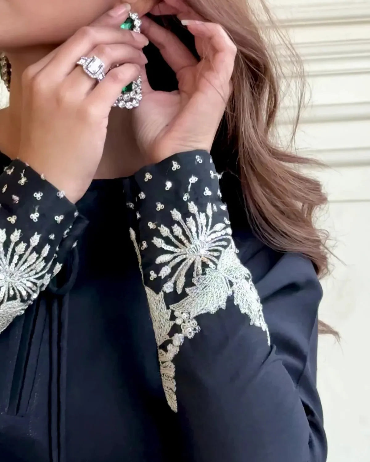 Close-up of a person wearing a black garment with white floral embroidery, holding a ring.