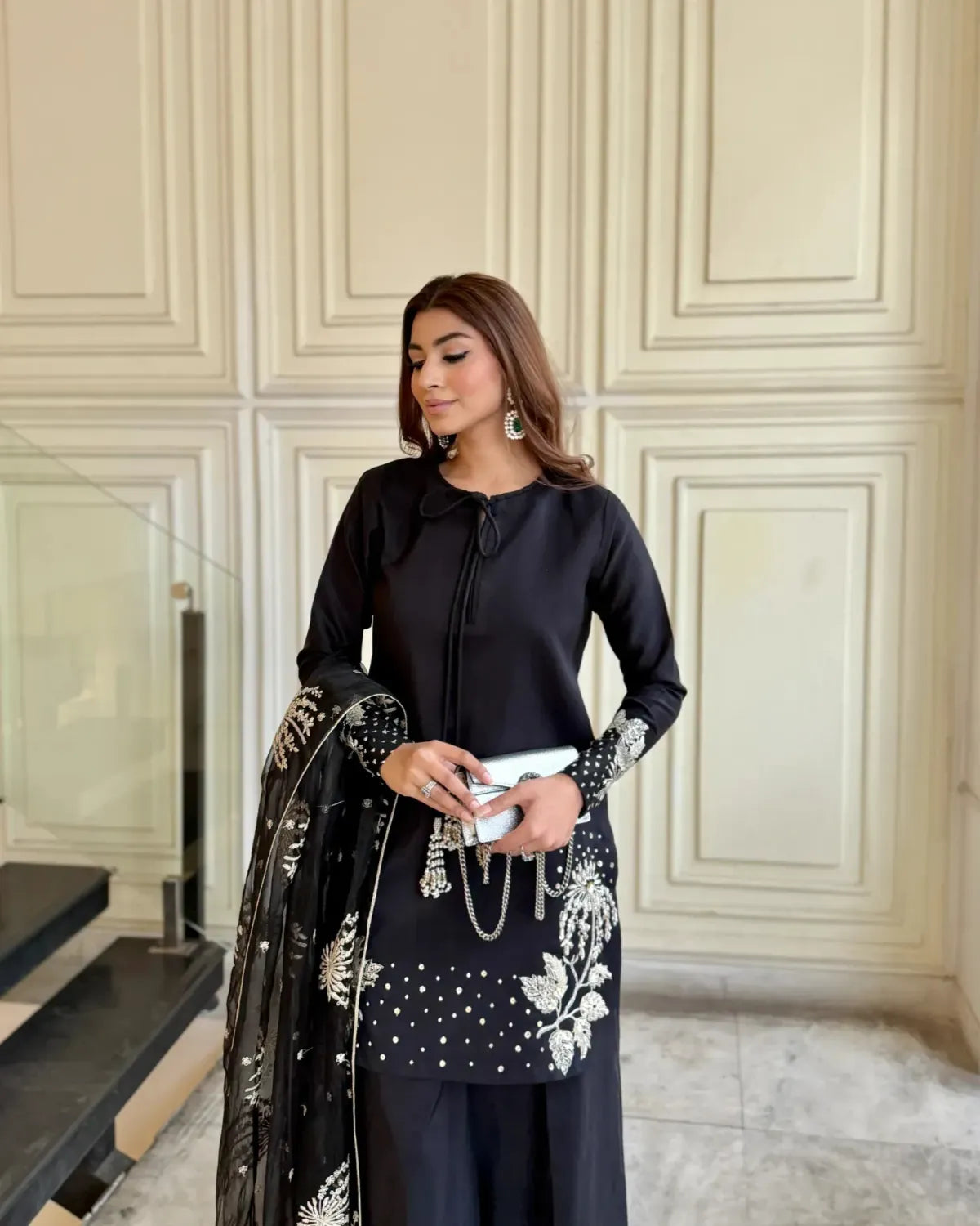 Woman in a black outfit with floral patterns standing in a room with decorative walls.