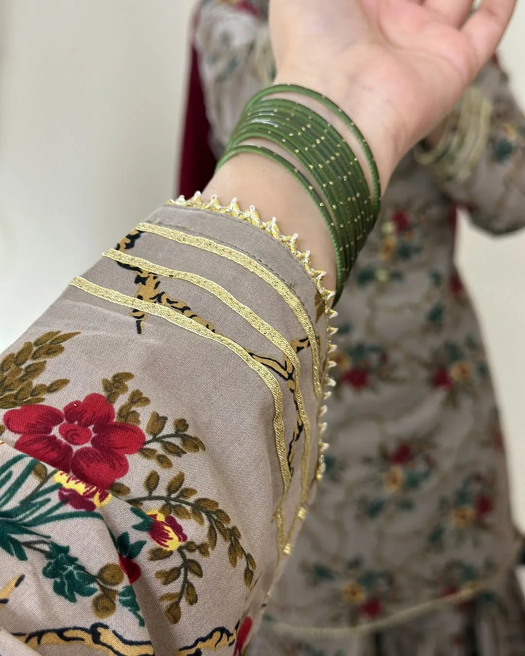 Close-up of a hand wearing a green bangle with gold detailing on a floral garment.