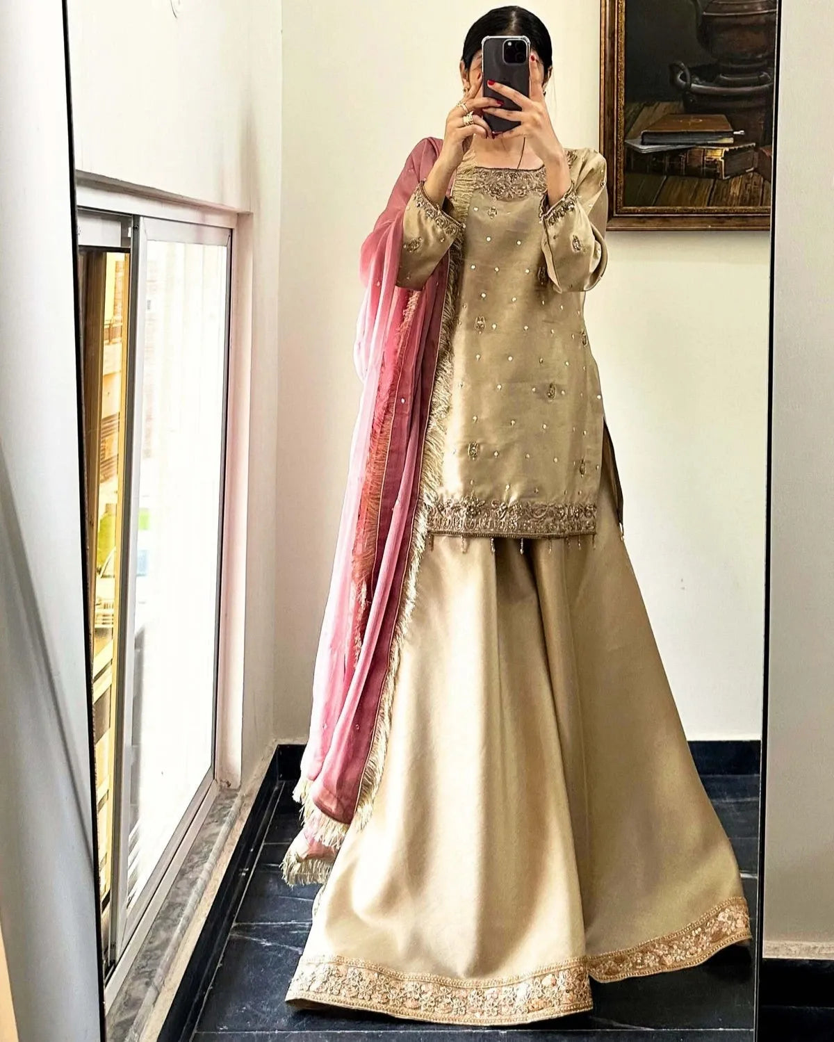 Person wearing a traditional outfit with a pink dupatta in front of a mirror.