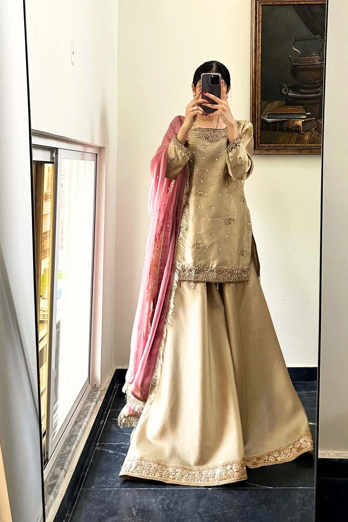 Person wearing a traditional outfit with a pink dupatta in a room.