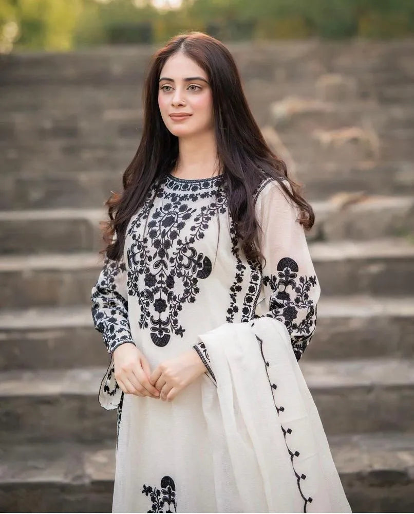 Woman in a white and black embroidered outfit standing on stone steps.