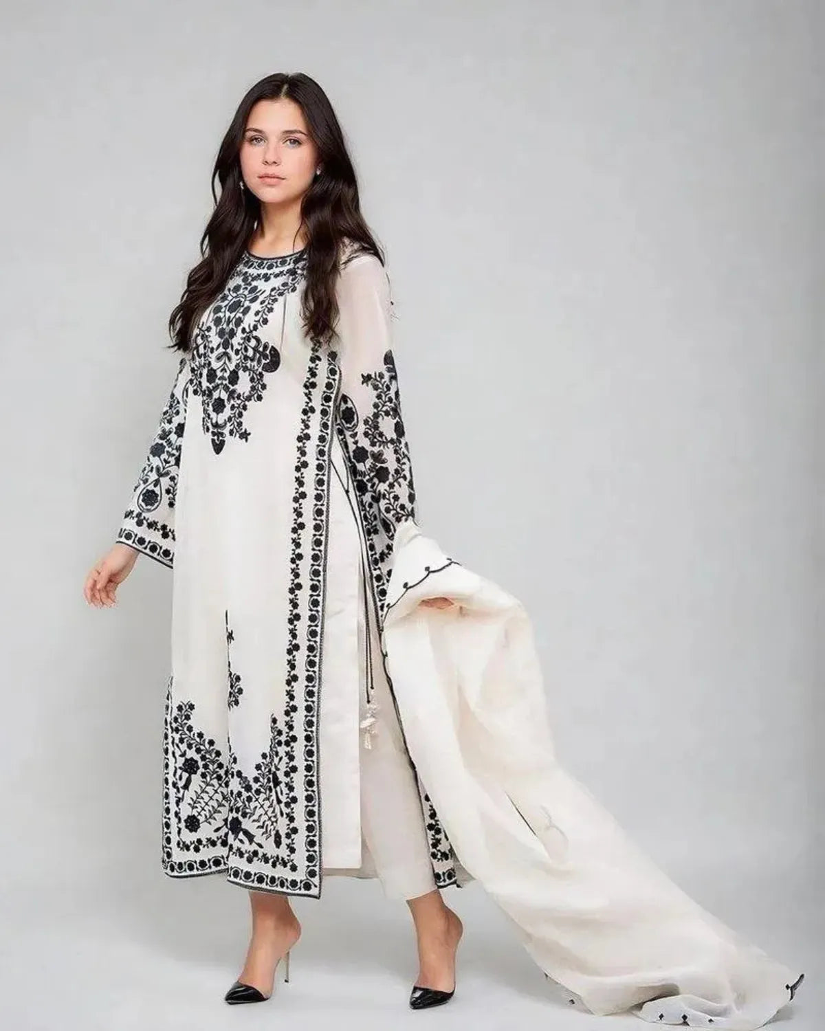 Woman wearing a white and black embroidered outfit on a gray background