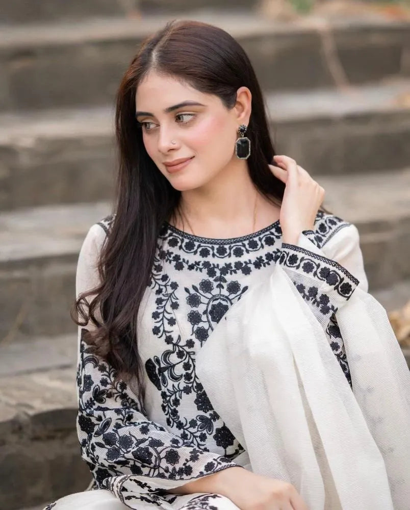 Woman wearing a black and white traditional outfit with a white dupatta, sitting on steps.