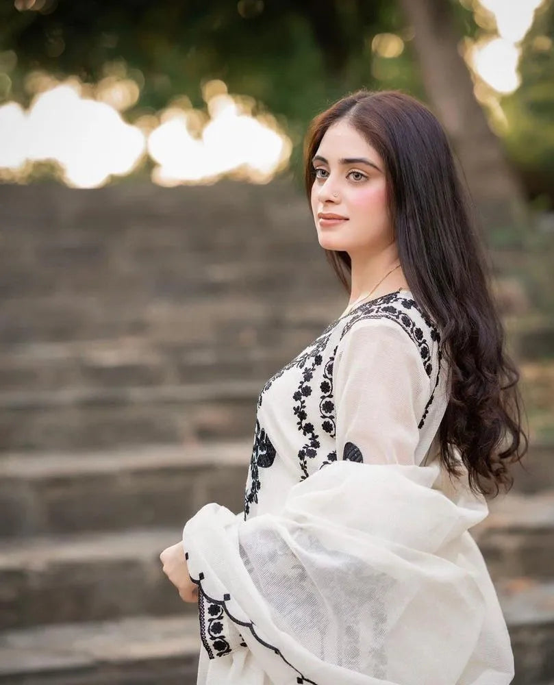 Woman in a white and black traditional outfit standing outdoors on stone steps.