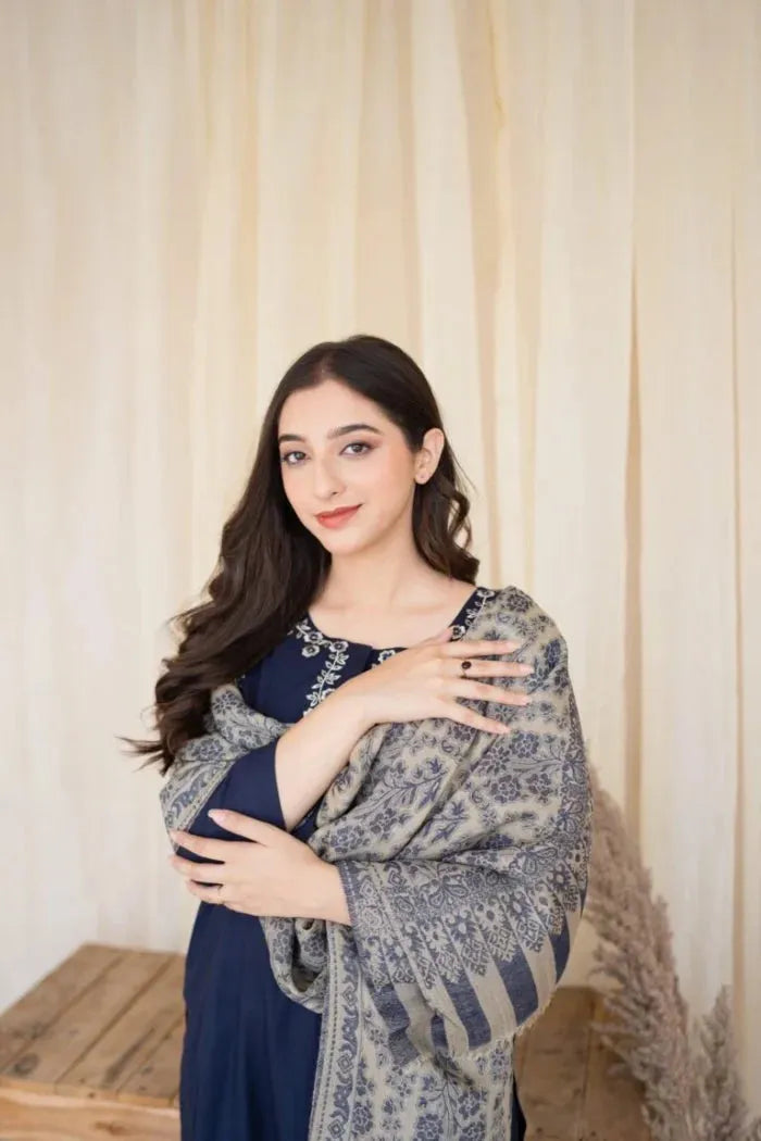 Woman wearing a blue dress with a floral shawl against a beige curtain background