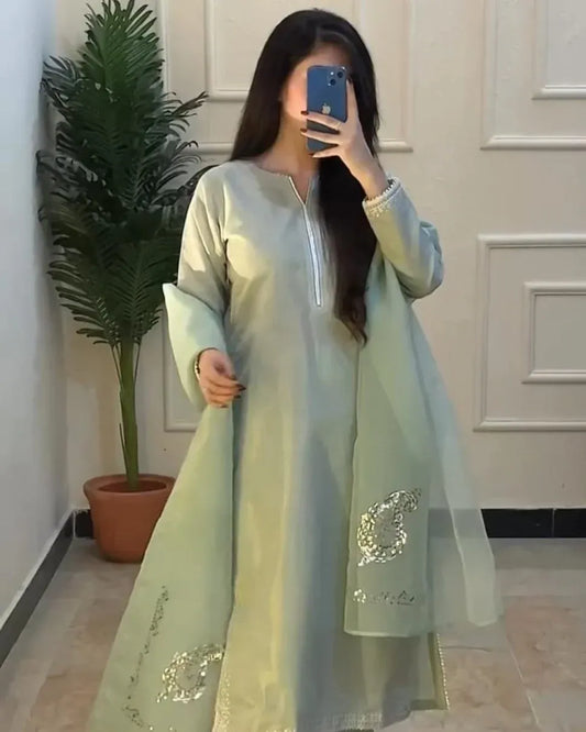 Person wearing a light green traditional outfit with embroidery, standing indoors.