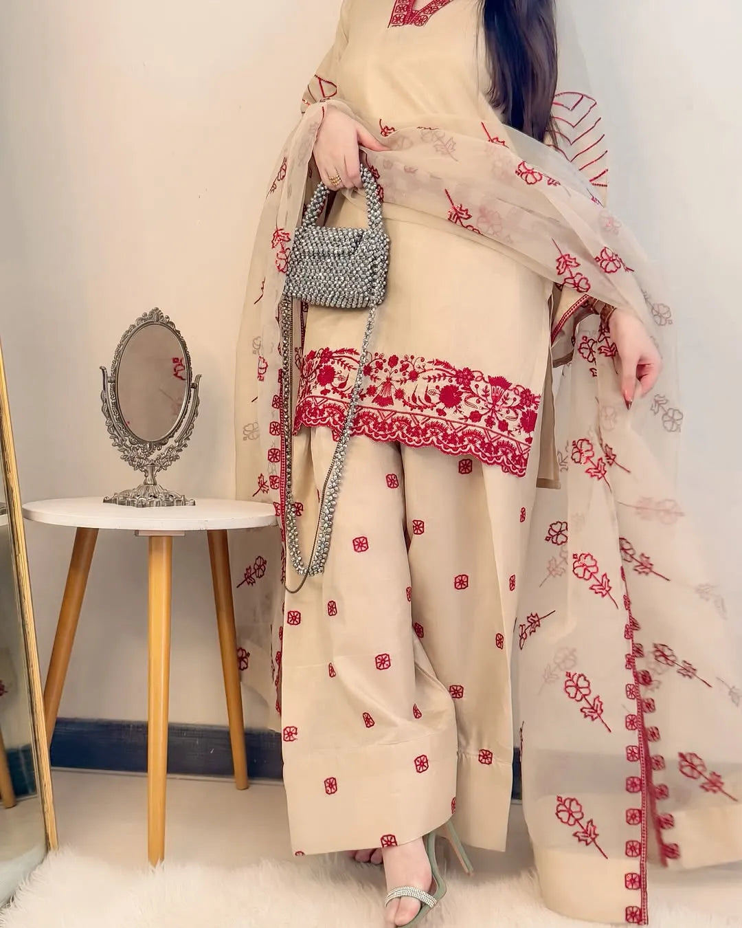 Person wearing a traditional outfit with red floral patterns in a room setting.