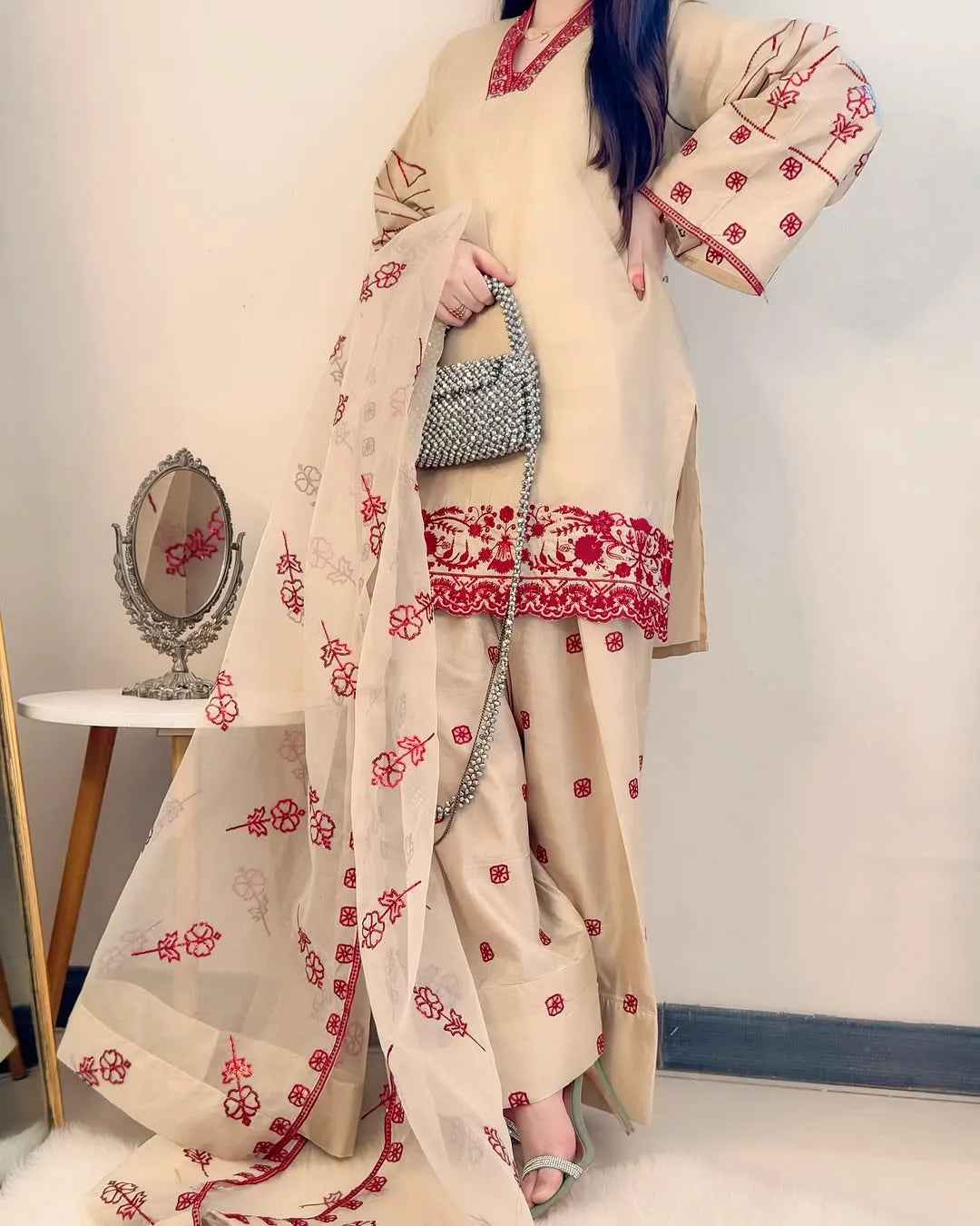 Woman wearing a beige outfit with red floral patterns, holding a matching shawl.