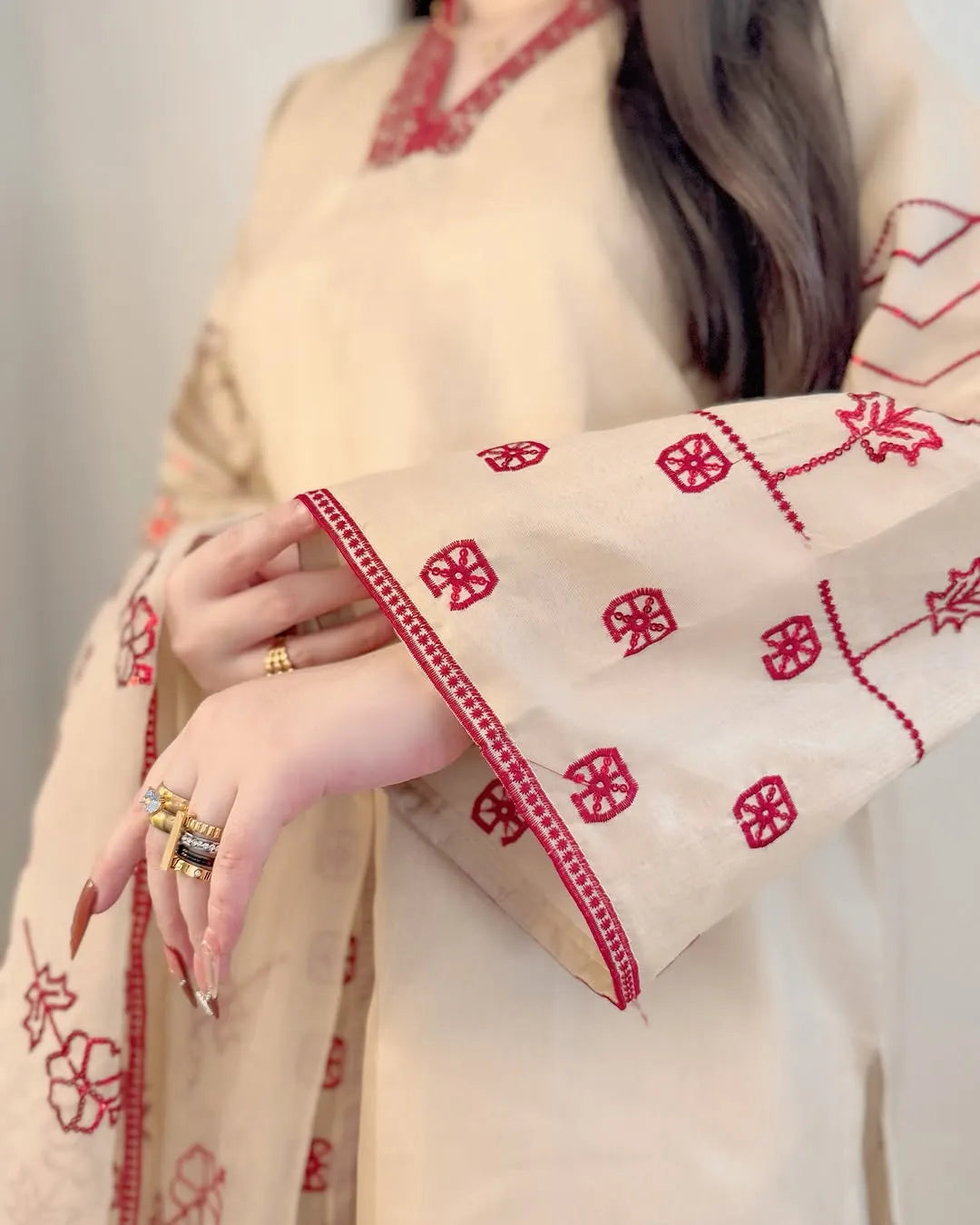 Beige fabric with red floral embroidery held by a person against a neutral background