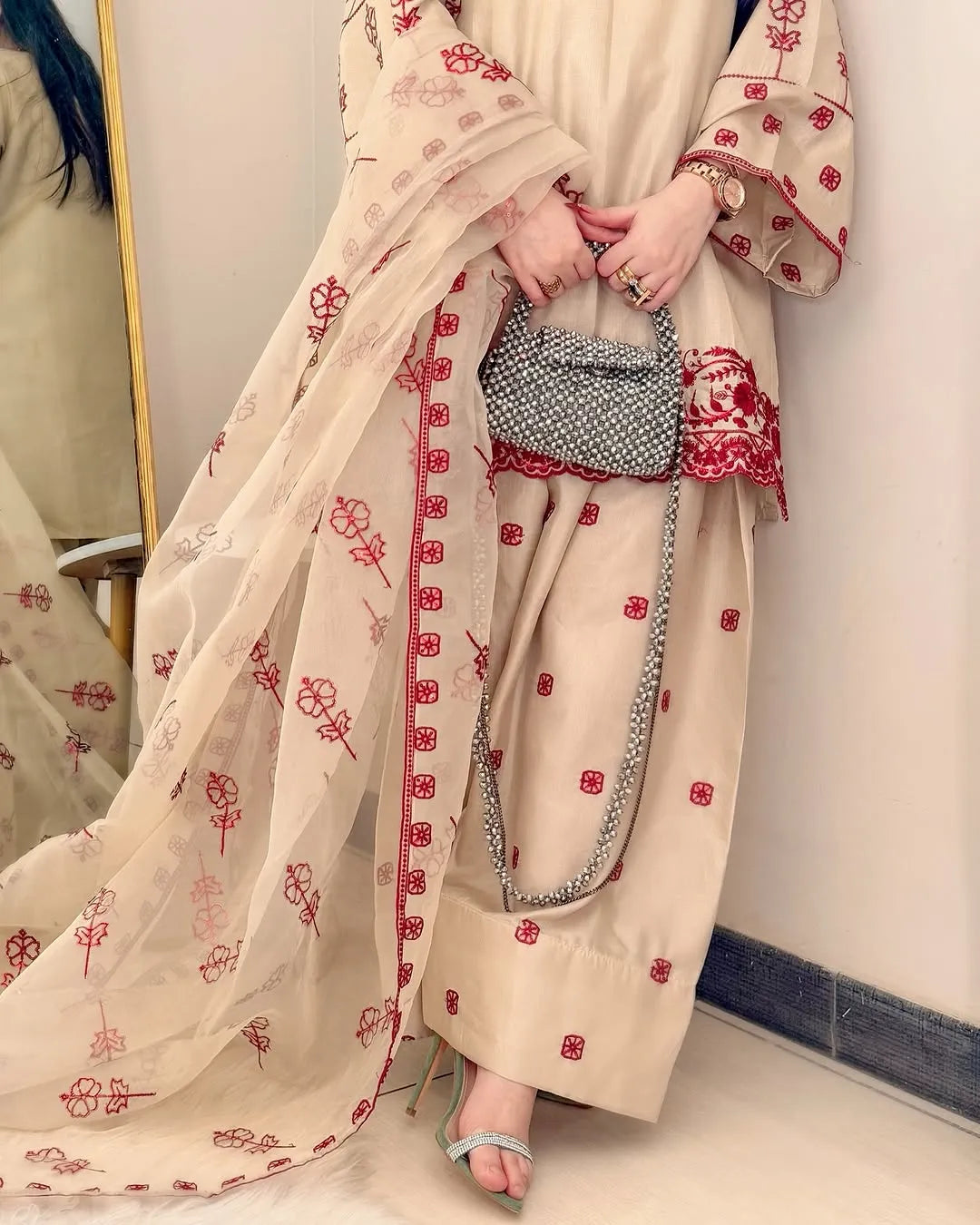 Person wearing a beige outfit with red floral patterns holding a silver handbag.