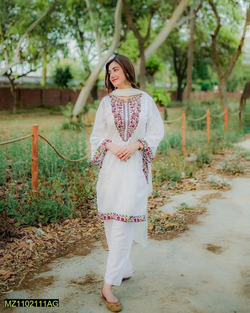 Woman in a white traditional outfit with floral patterns standing outdoors on a path.