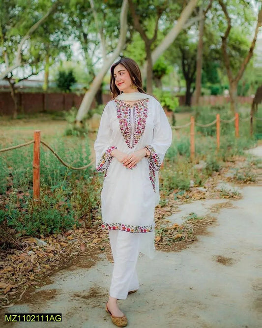 Woman in a white traditional outfit with floral patterns standing outdoors on a path.