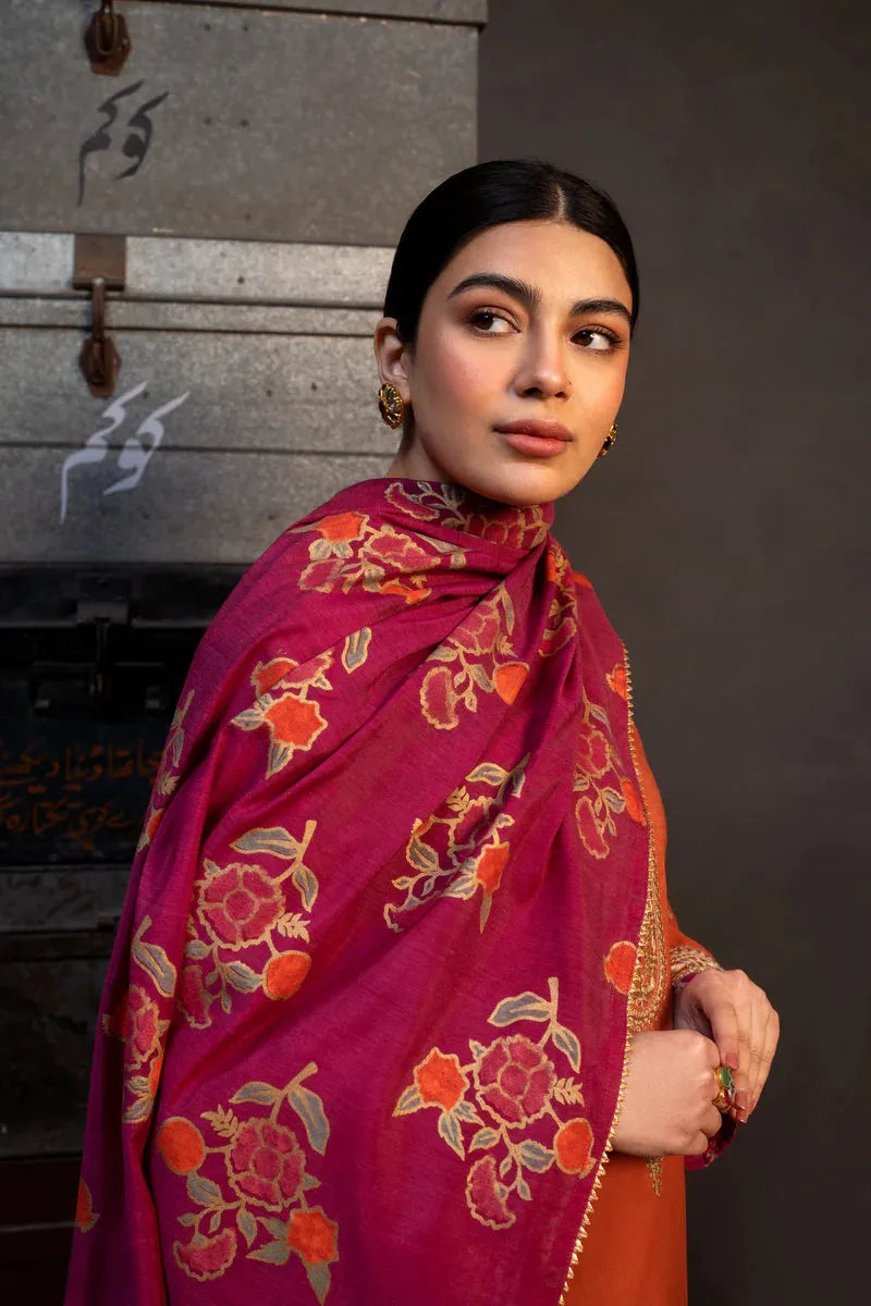 Woman wearing a vibrant pink and orange traditional outfit with floral patterns against a dark background.