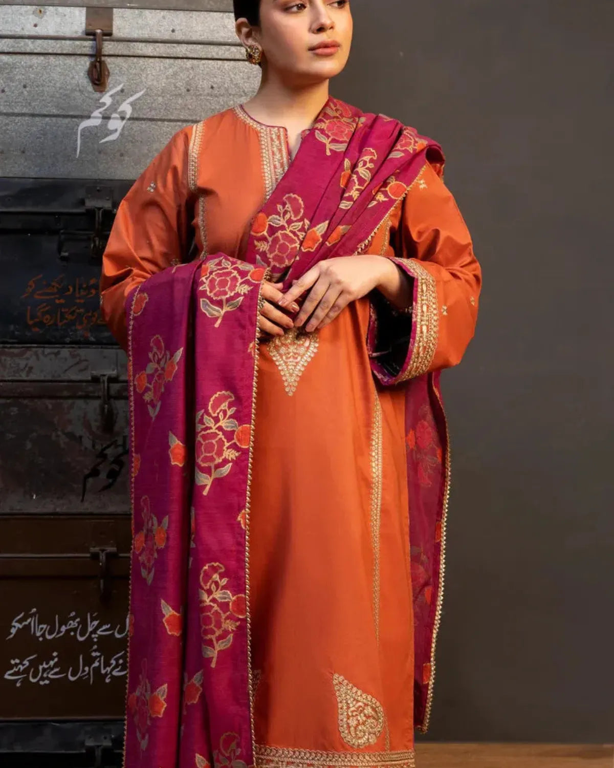 Woman wearing an orange and pink traditional outfit with floral patterns against a dark background.