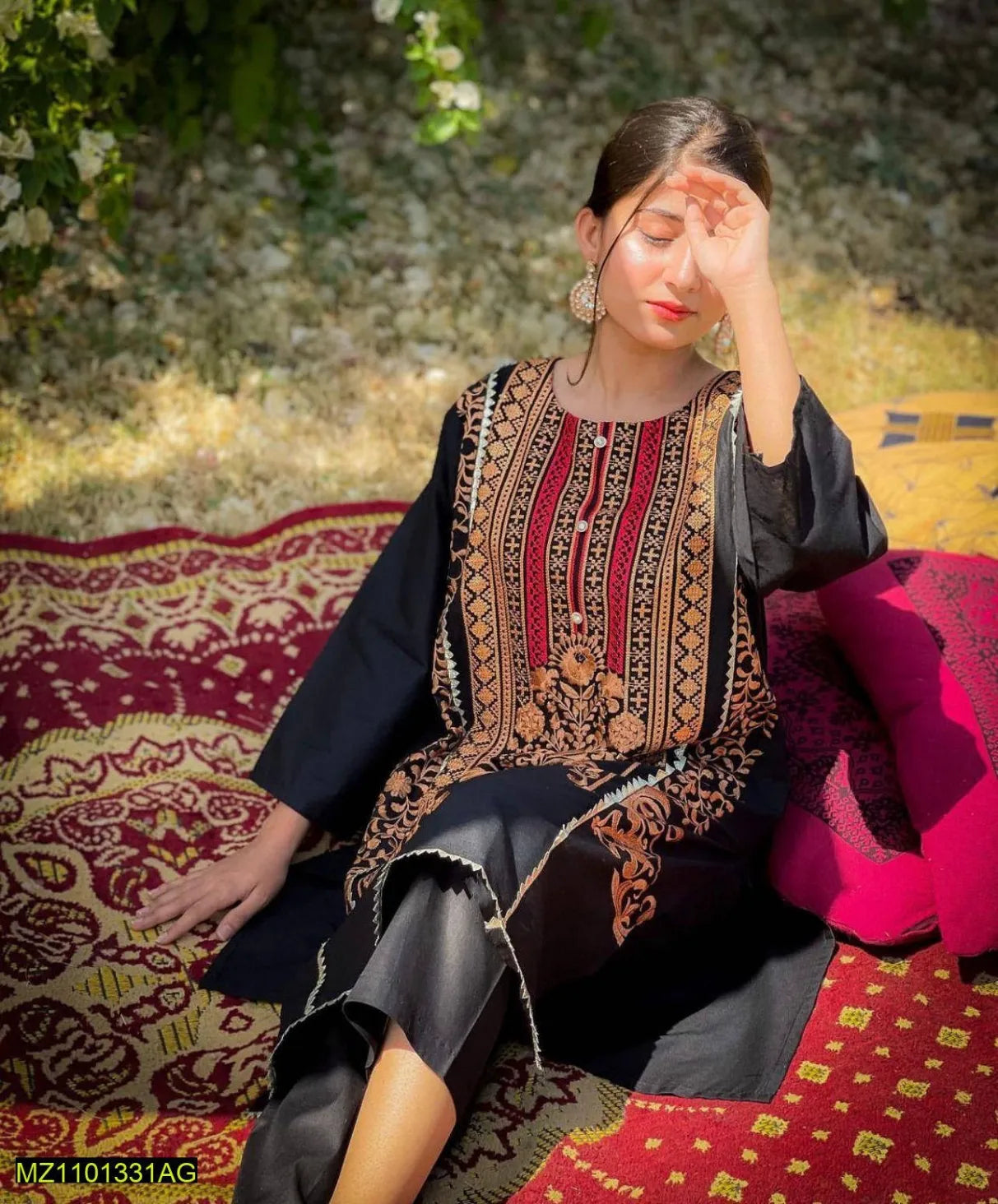 Woman in traditional embroidered outfit sitting on a patterned rug outdoors.