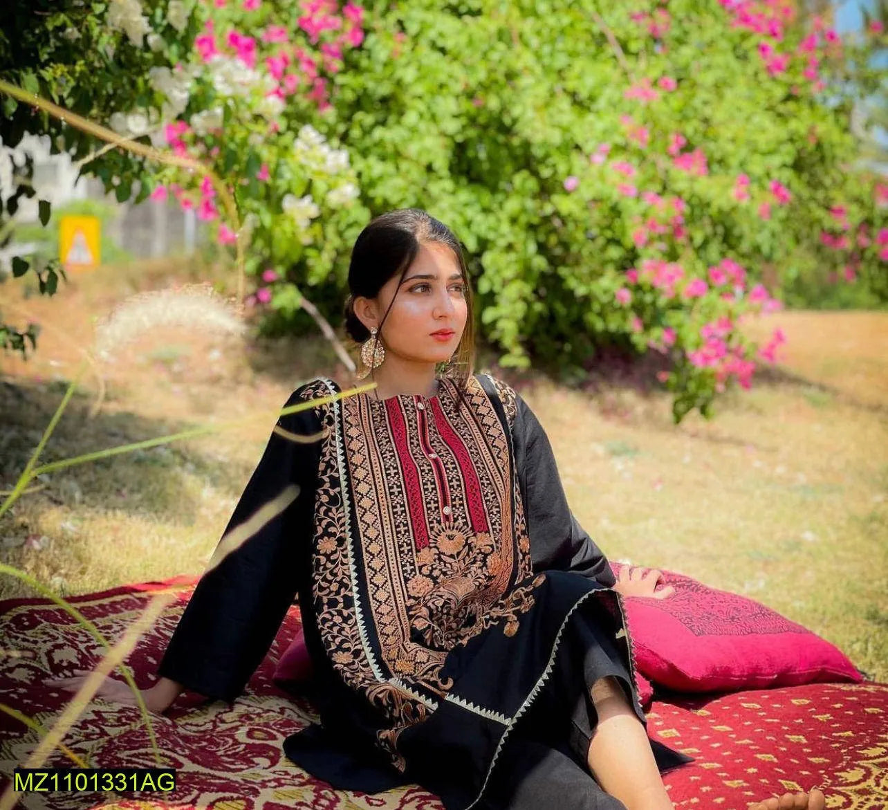 Woman sitting on a patterned mat in a garden with flowers and greenery.