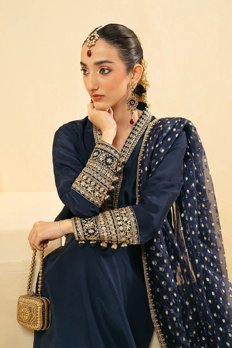 Woman in traditional navy blue outfit with gold embroidery and accessories on a beige background