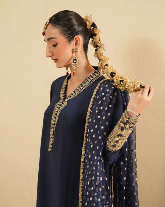 Woman wearing a navy blue traditional outfit with gold embroidery against a beige background