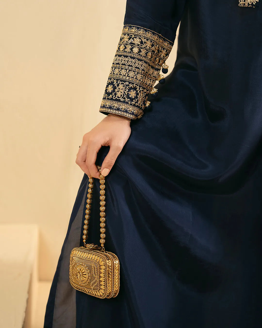 Person wearing a dark blue embroidered garment holding a gold handbag.