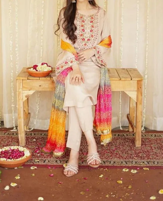 Woman sitting on a wooden bench wearing a floral embroidered outfit with a colorful scarf.